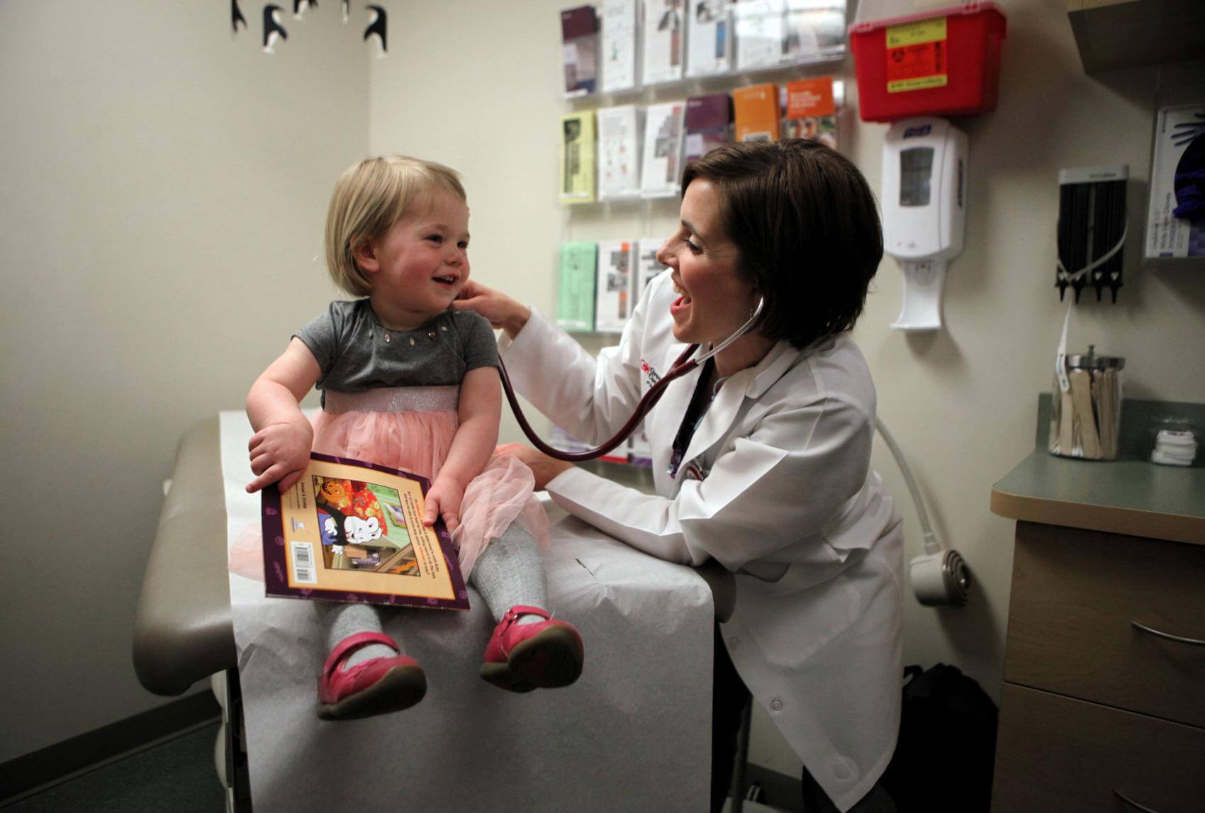 Toddler at well-child visits at doctor's office receiving a book from her provider. Reading programs often are supporting of parents and children.